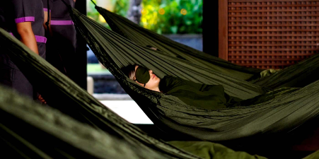 Person resting in a dark green hammock with an eye mask in a tranquil wellness setting, part of the JIWA relaxation experience at Conrad Bali.