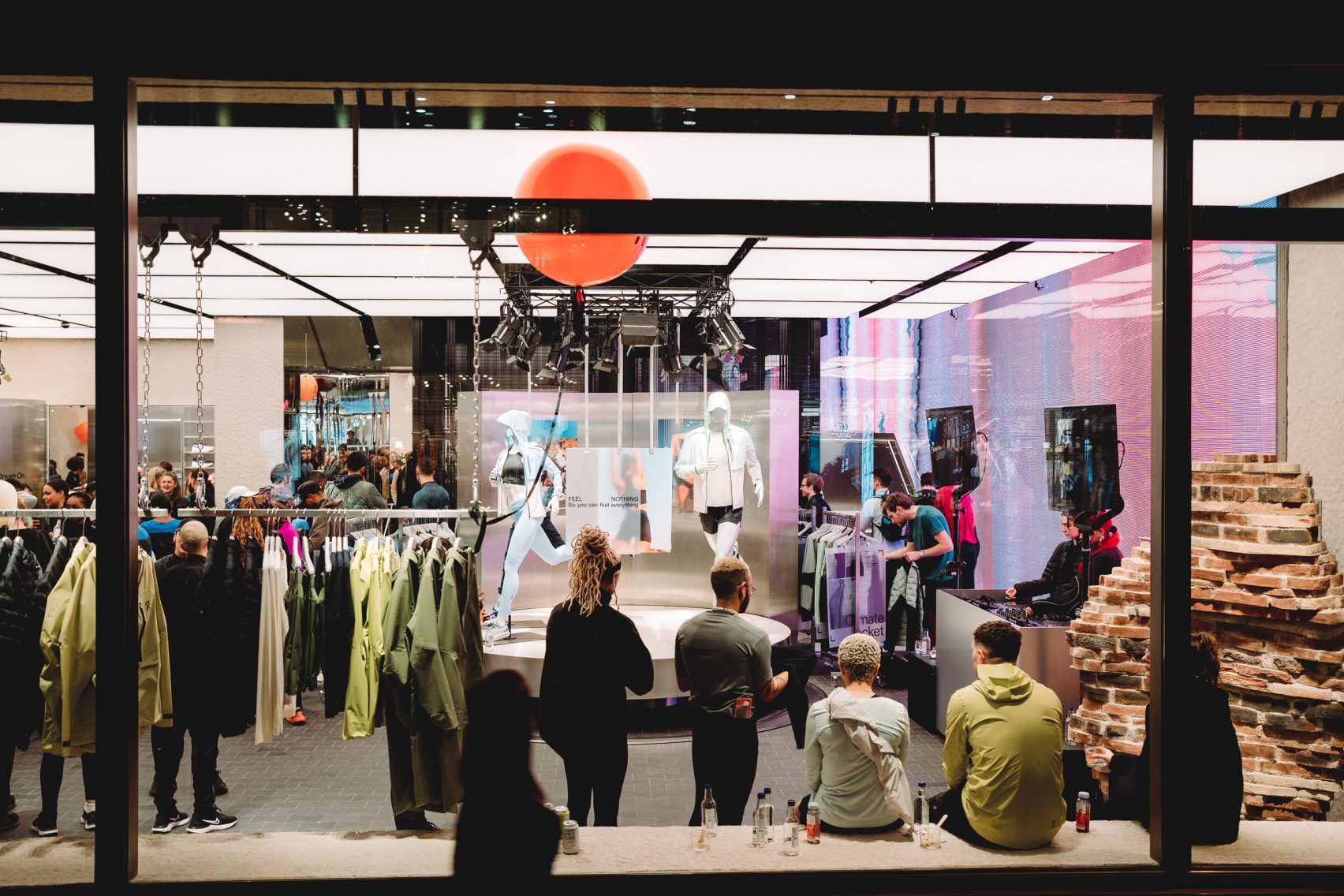 Crowds gather inside On Running’s flagship store in London, featuring illuminated retail displays, mannequins in motion, and a curated streetwear-meets-sport atmosphere.