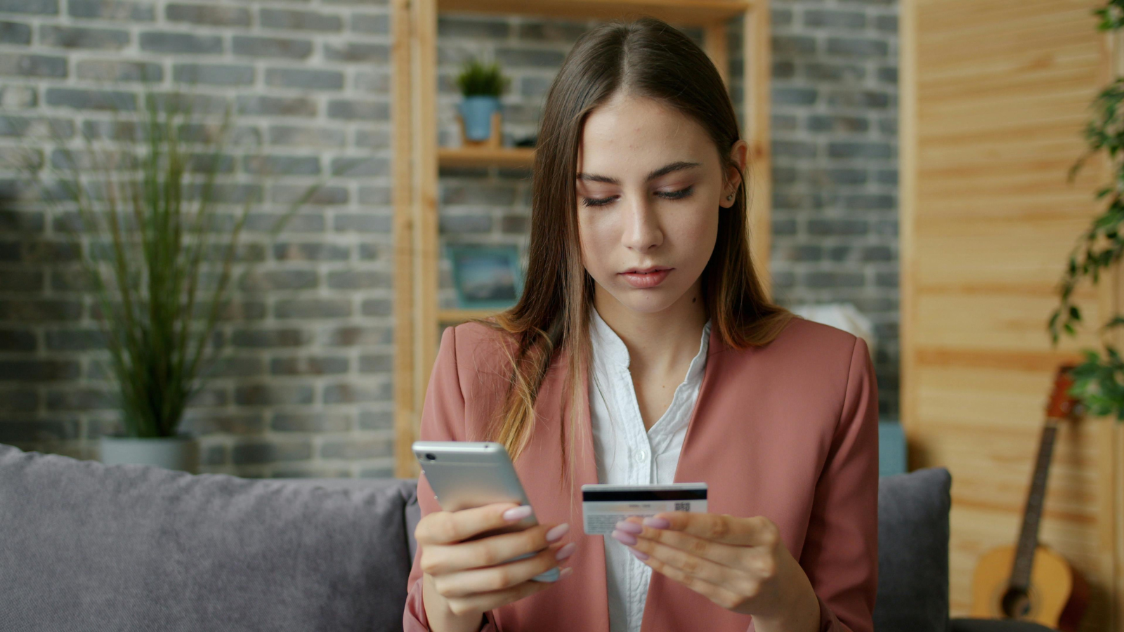 A woman in business attire looking at a phone and holding a credit card