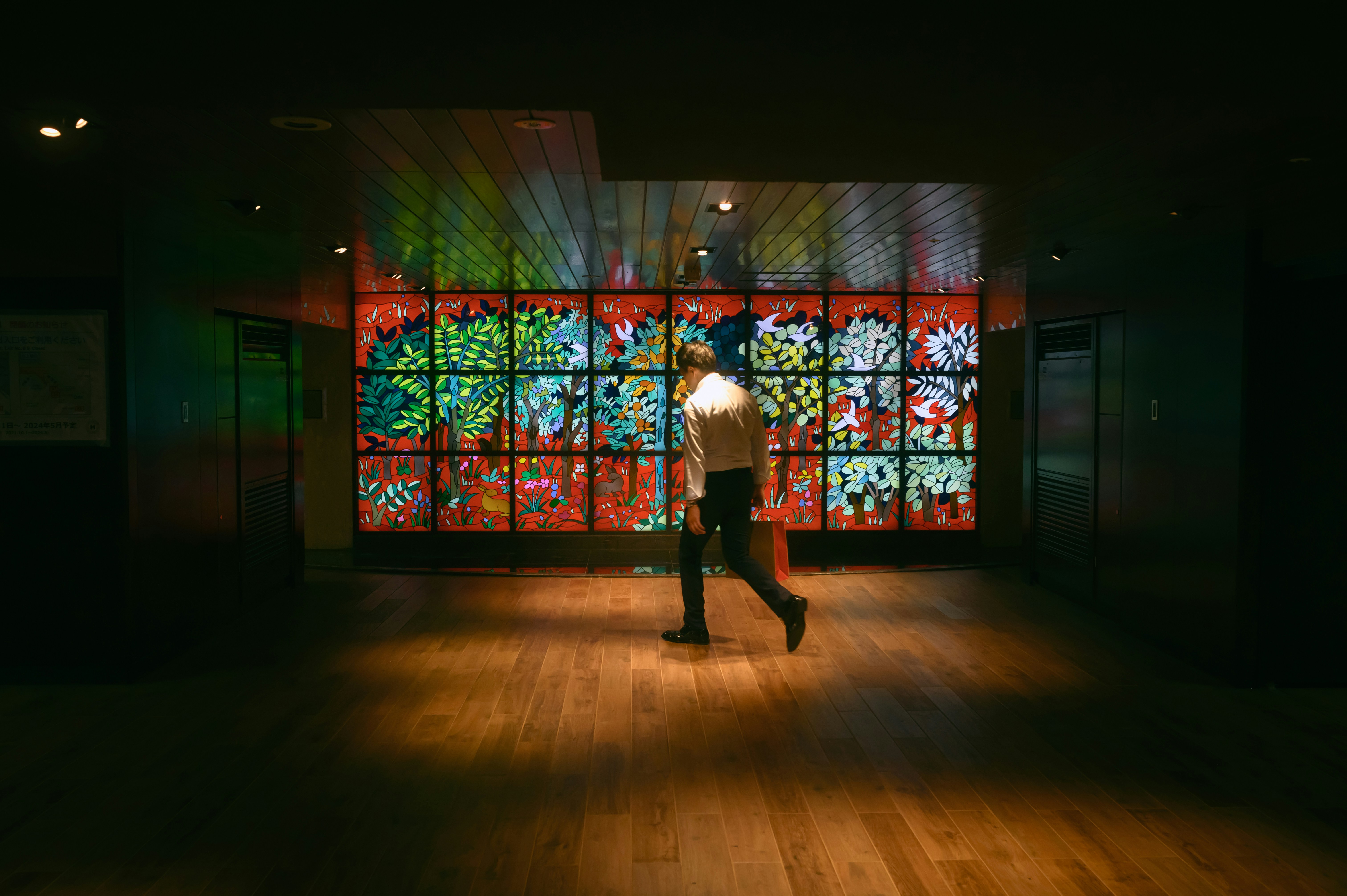 Man walking through dimly lit room backlit by a Japanese floral artwork
