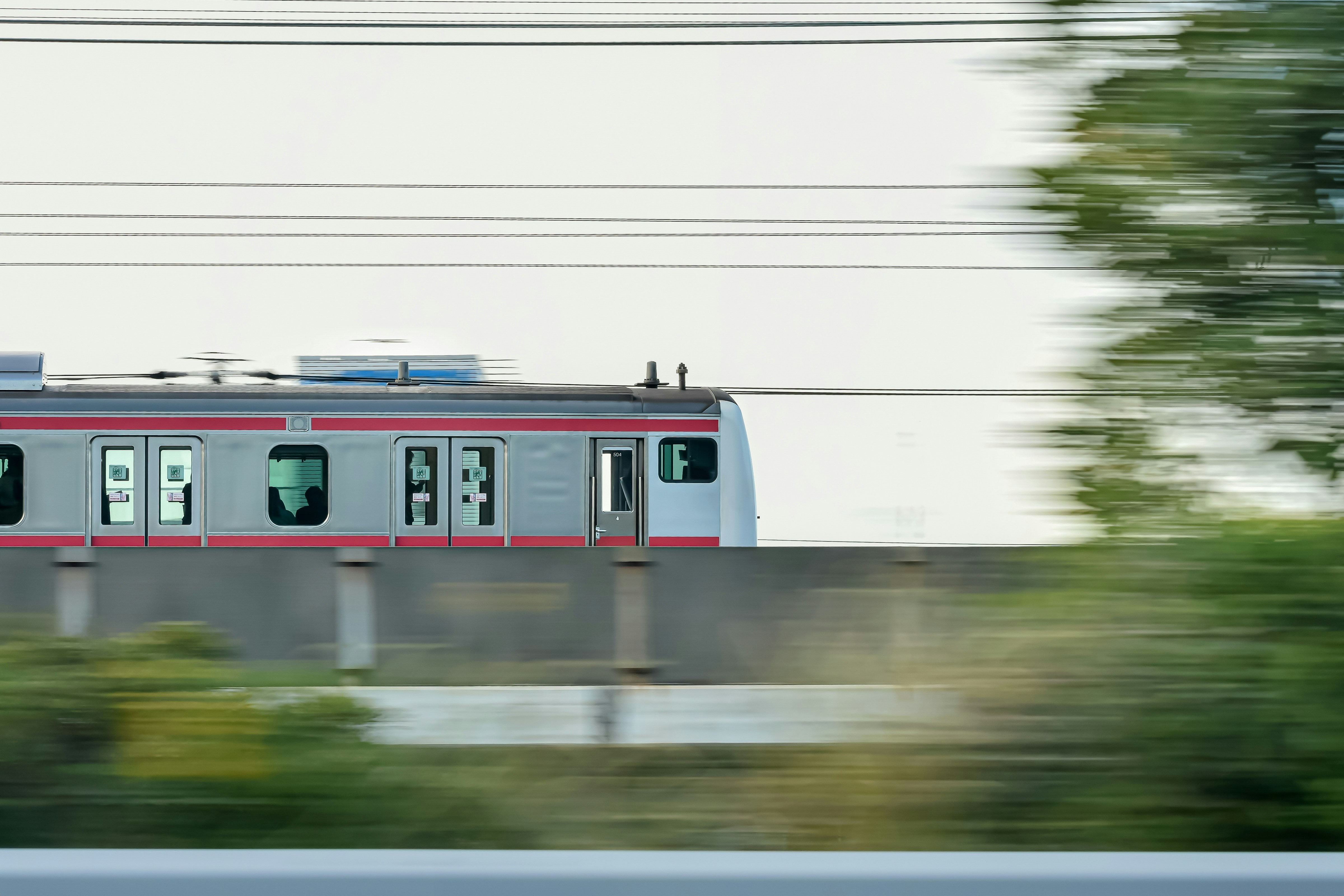 Japanese Subway Train going over bridge above and surrounded by green trees