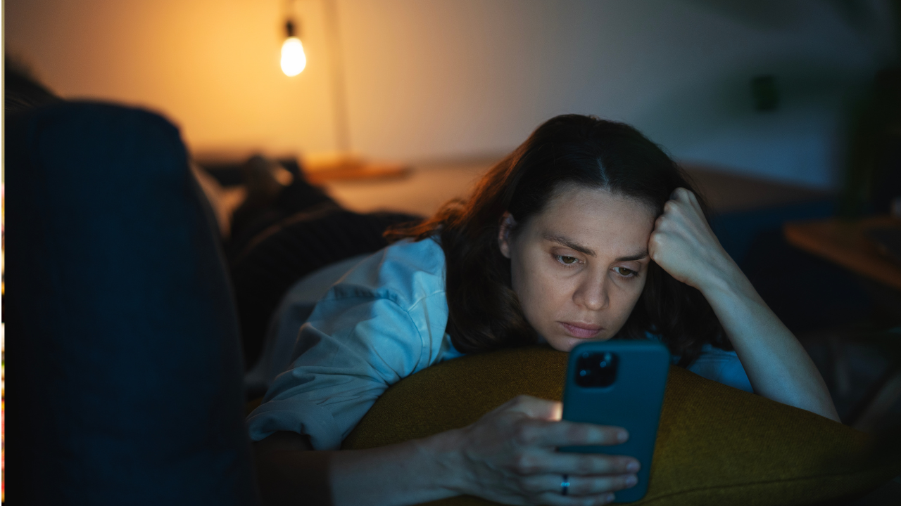 Lone, tired woman staring at her phone on a dim-lit couch.
