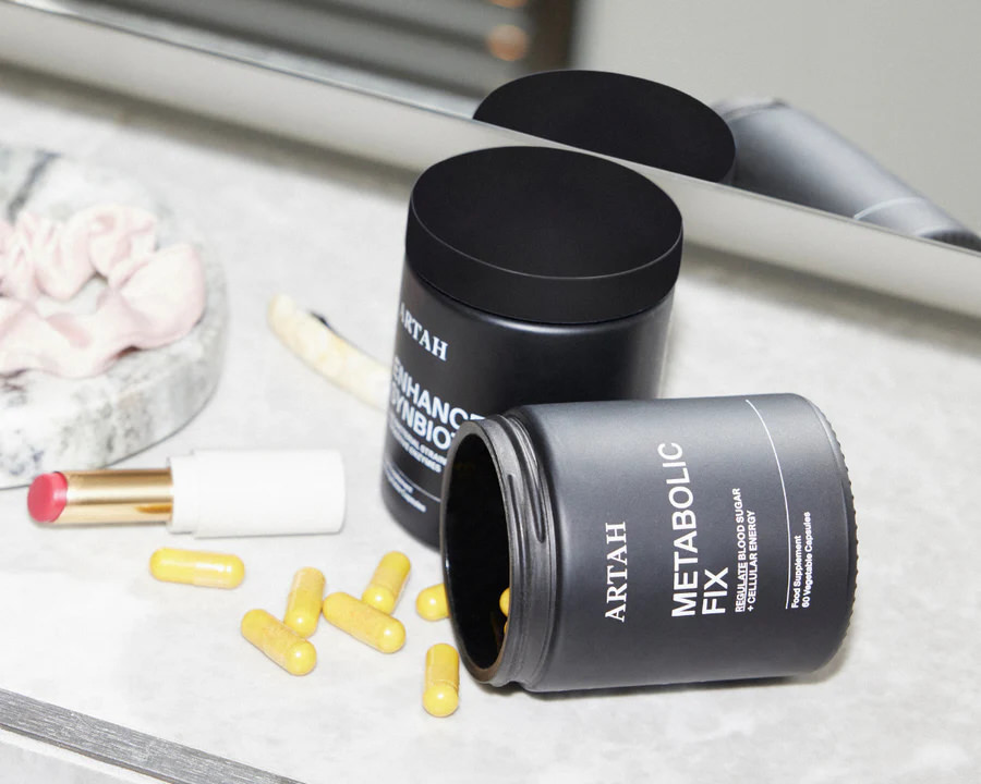 Artah supplements on a counter, with yellow capsules spilled from an open Metabolic Fix bottle.